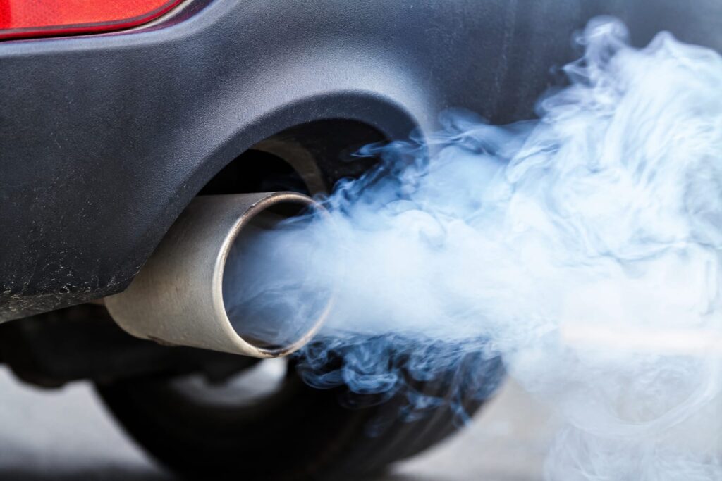 Close-up of white/blue smoke from a tailpipe, daylight, engine bay or rear of car in frame